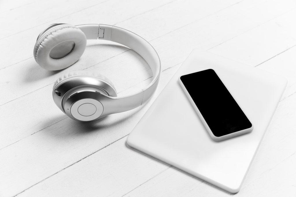 Kopfhörer, Smartphone und Tablet liegen nebeneinander auf einem hellen Untergrund