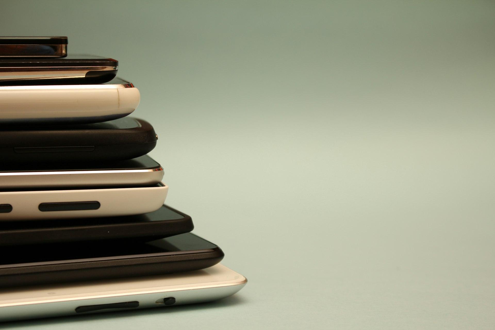 Gestapelte gebrauchte Smartphones verschiedener Modelle als Sinnbild für An- und Verkauf